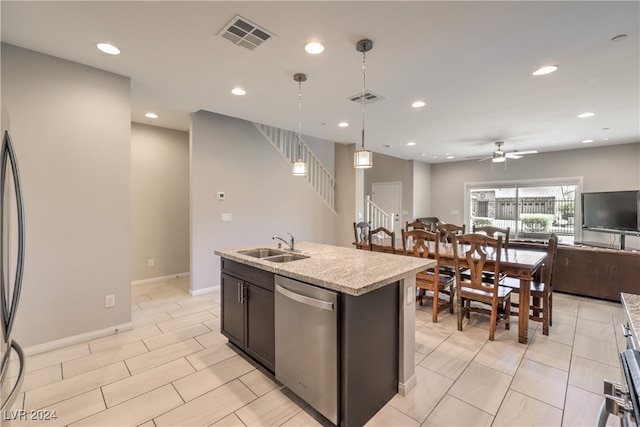 kitchen with ceiling fan, stainless steel dishwasher, hanging light fixtures, a kitchen island with sink, and light stone countertops