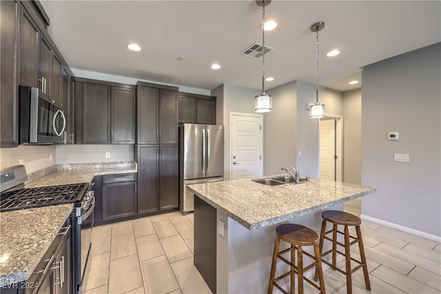 kitchen with sink, stainless steel appliances, decorative light fixtures, and an island with sink