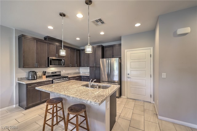 kitchen featuring appliances with stainless steel finishes, light stone counters, sink, decorative light fixtures, and a breakfast bar area