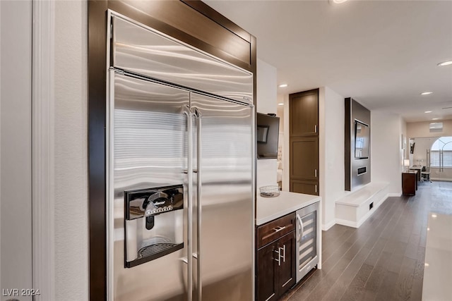 kitchen with beverage cooler, dark wood-style flooring, built in refrigerator, light countertops, and dark brown cabinets