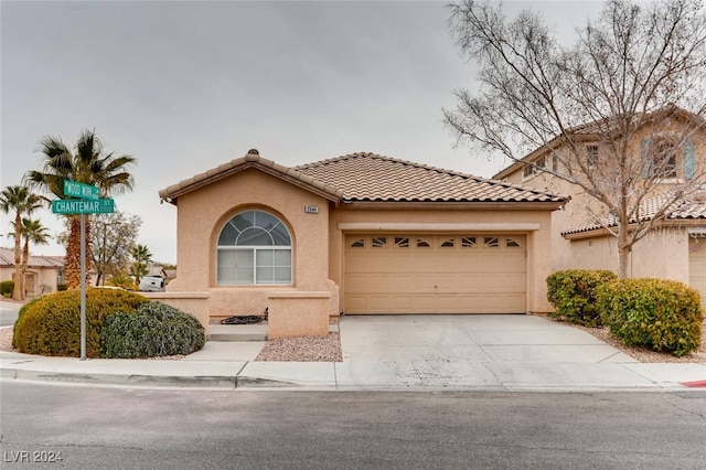 mediterranean / spanish house with driveway, an attached garage, a tiled roof, and stucco siding