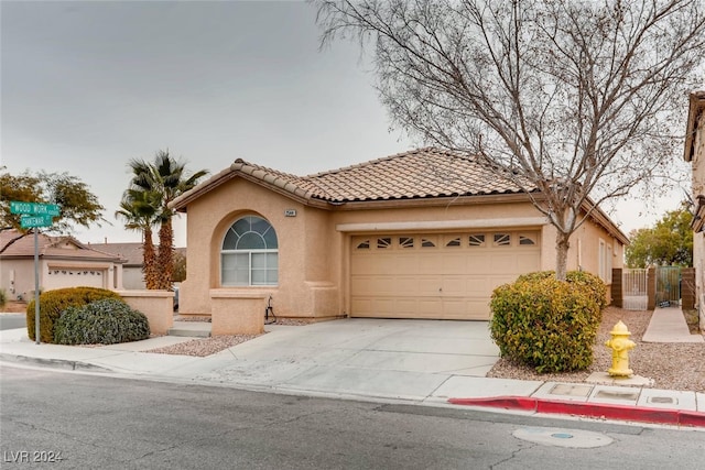 mediterranean / spanish home featuring a garage, driveway, a tiled roof, and stucco siding