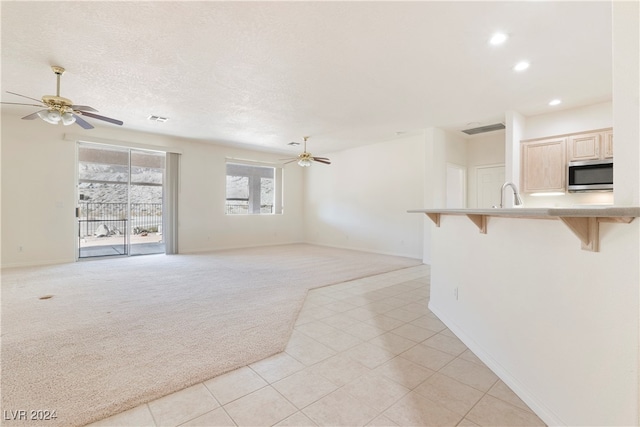 unfurnished living room with sink, ceiling fan, and light carpet