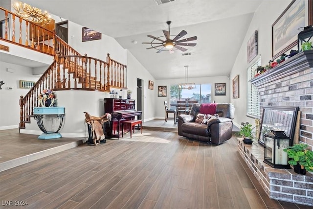 living area featuring a brick fireplace, baseboards, stairs, ceiling fan with notable chandelier, and wood finished floors