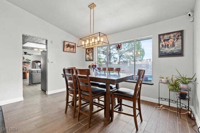 dining area featuring vaulted ceiling, ceiling fan with notable chandelier, baseboards, and wood finished floors