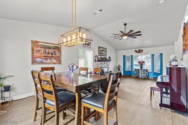 dining space featuring visible vents, a ceiling fan, a fireplace, wood tiled floor, and vaulted ceiling