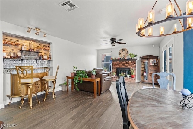 dining area with visible vents, a bar, a brick fireplace, and wood finished floors