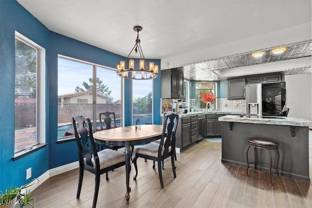 dining room with a notable chandelier, light wood-style flooring, baseboards, and a healthy amount of sunlight