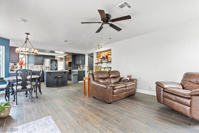 living area featuring visible vents, baseboards, wood finished floors, and ceiling fan with notable chandelier