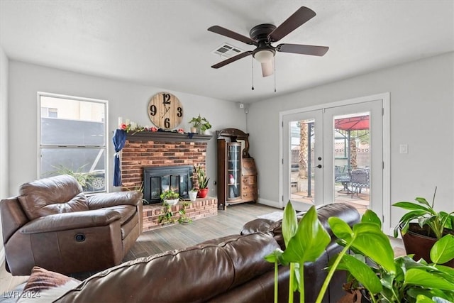 living area featuring visible vents, a brick fireplace, french doors, wood finished floors, and a ceiling fan