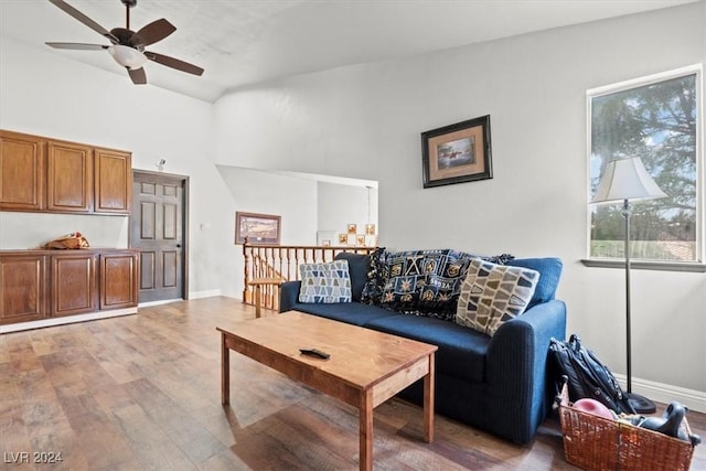 living room with a towering ceiling, a ceiling fan, baseboards, and wood finished floors