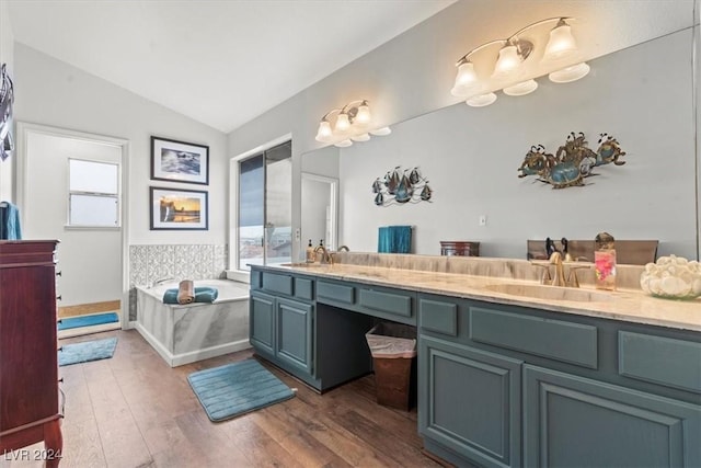 full bathroom featuring lofted ceiling, double vanity, hardwood / wood-style floors, a bath, and a sink