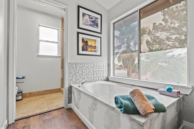 full bathroom with a garden tub, wood finished floors, and baseboards