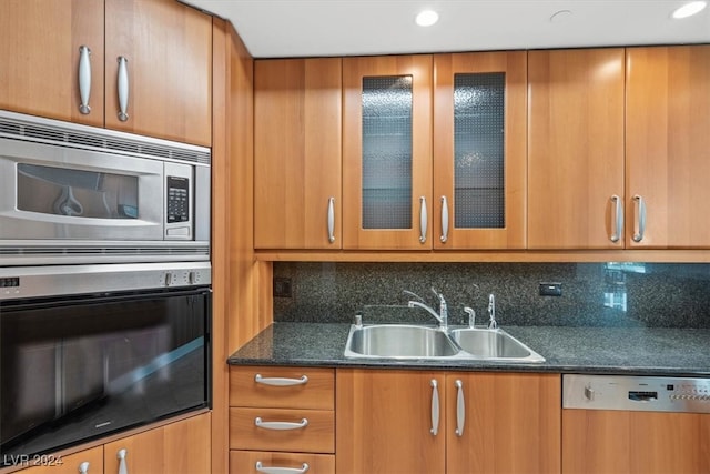 kitchen with stainless steel appliances, sink, decorative backsplash, and dark stone counters