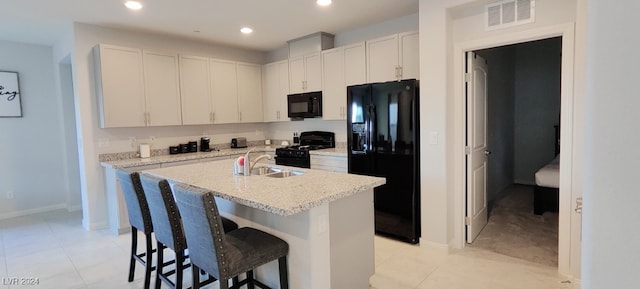 kitchen with light stone counters, a breakfast bar area, white cabinets, black appliances, and a center island with sink