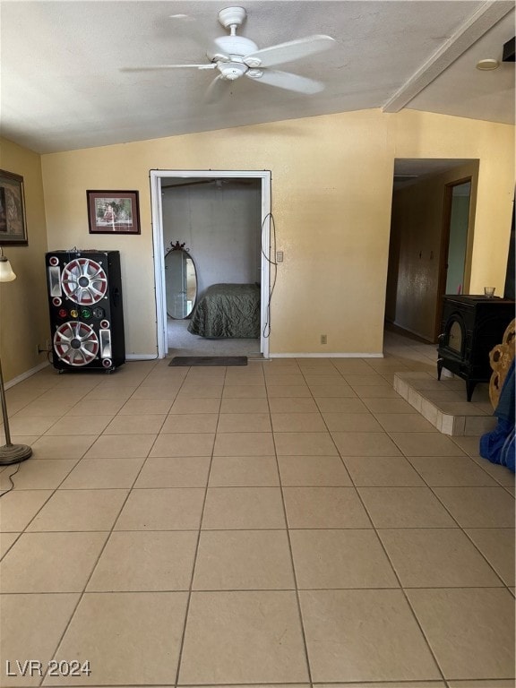 unfurnished living room featuring ceiling fan, tile patterned flooring, vaulted ceiling, and a wood stove