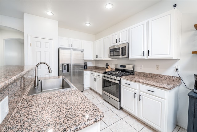 kitchen with appliances with stainless steel finishes, light stone counters, sink, white cabinetry, and light tile patterned flooring