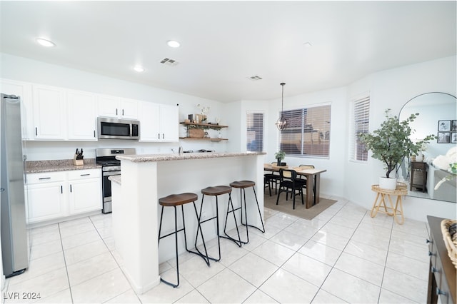 kitchen with a center island, light stone countertops, appliances with stainless steel finishes, decorative light fixtures, and white cabinetry