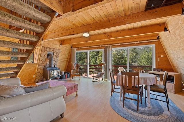 dining area with wood ceiling, a wood stove, wooden walls, beamed ceiling, and light wood-type flooring