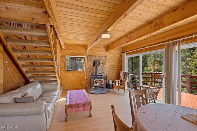 living room featuring wood walls, wood ceiling, a wood stove, beamed ceiling, and light hardwood / wood-style floors