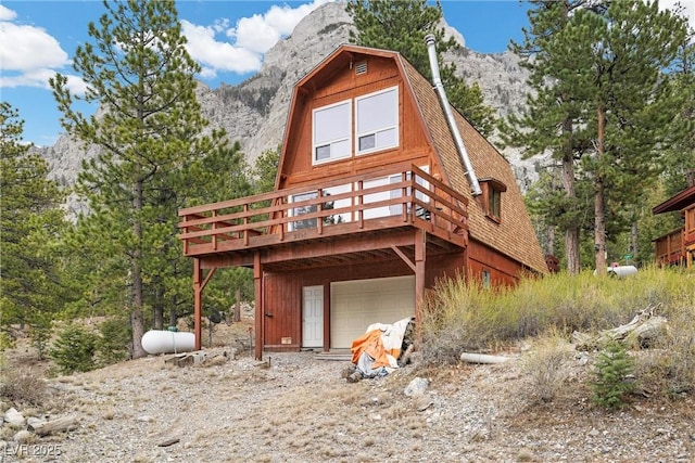 rear view of property featuring a deck with mountain view, a gambrel roof, and a garage