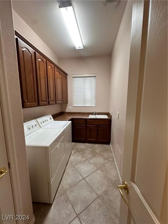 laundry area with cabinets, independent washer and dryer, light tile patterned floors, sink, and a textured ceiling