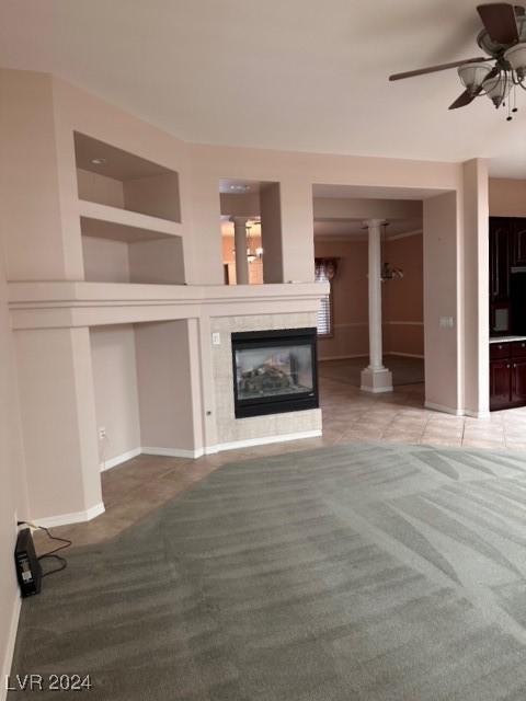 unfurnished living room with ceiling fan, light carpet, a fireplace, and ornate columns