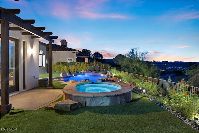 pool at dusk with an in ground hot tub and a yard