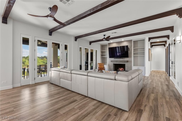 unfurnished living room featuring built in features, light wood-type flooring, beamed ceiling, french doors, and ceiling fan