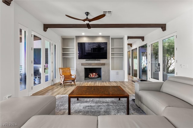 living room with light hardwood / wood-style flooring, beam ceiling, french doors, ceiling fan, and a premium fireplace