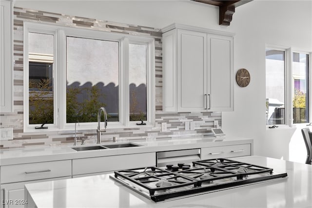 kitchen with white cabinetry, backsplash, sink, and stainless steel dishwasher