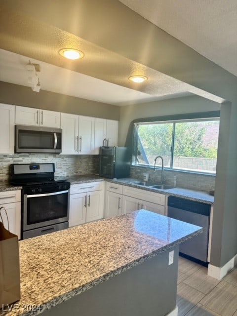 kitchen with white cabinetry, tasteful backsplash, light stone countertops, stainless steel appliances, and sink