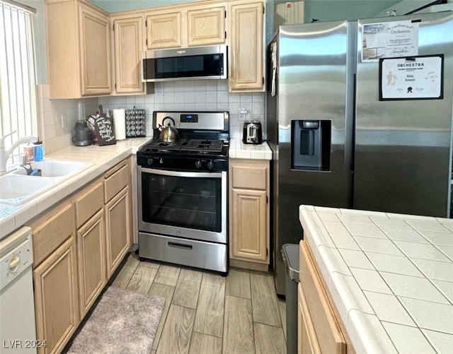 kitchen with sink, light hardwood / wood-style flooring, tile counters, tasteful backsplash, and stainless steel appliances