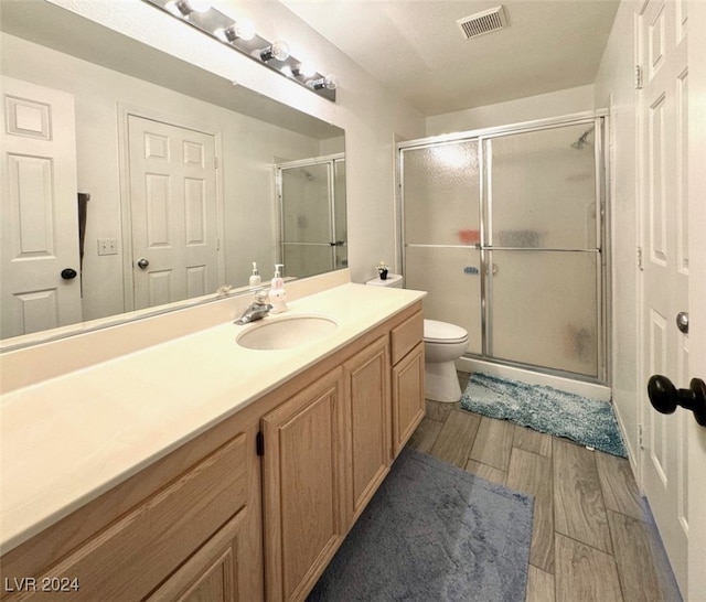 bathroom featuring wood-type flooring, a shower with door, vanity, and toilet