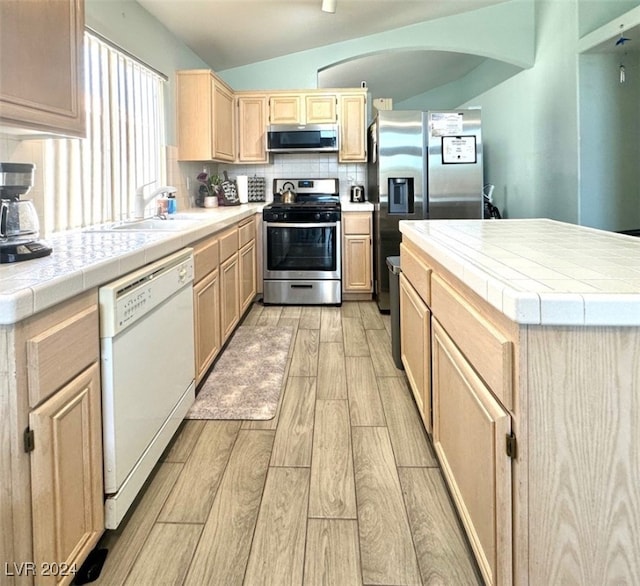 kitchen featuring backsplash, stainless steel appliances, light hardwood / wood-style flooring, sink, and tile counters