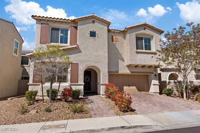 mediterranean / spanish-style home featuring an attached garage, a tile roof, decorative driveway, and stucco siding