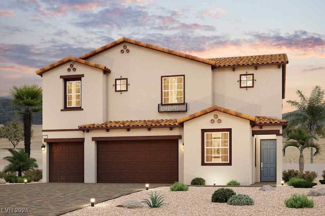 mediterranean / spanish-style house with a garage, a tiled roof, decorative driveway, and stucco siding