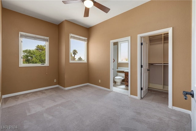 unfurnished bedroom with ceiling fan, ensuite bathroom, light carpet, a walk in closet, and a closet