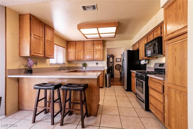 1834 Escondido Ter, Henderson, NV 89074 - kitchen featuring visible vents, a peninsula, a breakfast bar area, black microwave, and stainless steel range with gas stovetop