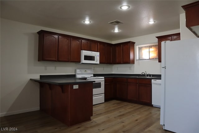 kitchen with hardwood / wood-style floors, sink, a kitchen breakfast bar, kitchen peninsula, and white appliances