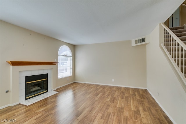 unfurnished living room with light wood-type flooring and a tiled fireplace