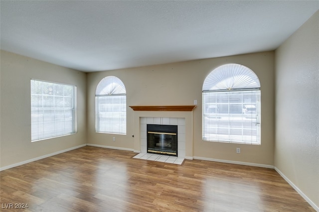 unfurnished living room with a healthy amount of sunlight, a tile fireplace, and light hardwood / wood-style floors