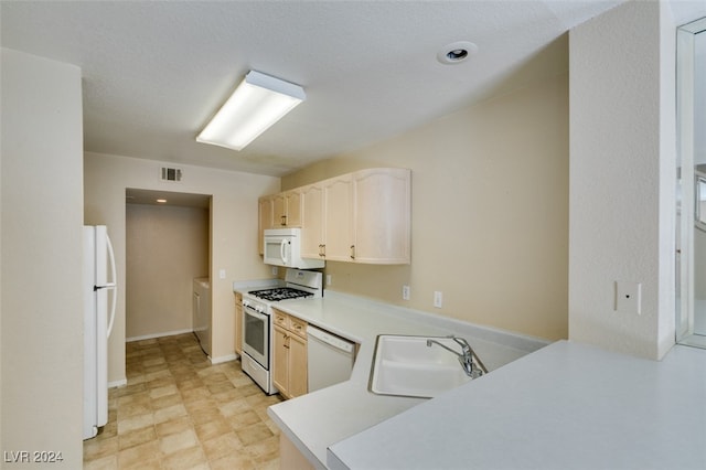 kitchen featuring white appliances, independent washer and dryer, light tile patterned floors, kitchen peninsula, and sink