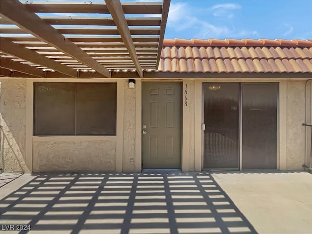 doorway to property featuring a patio, stucco siding, a tile roof, and a pergola