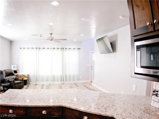 kitchen featuring light wood finished floors, visible vents, stainless steel microwave, light stone countertops, and open floor plan