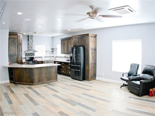 kitchen with fridge with ice dispenser, visible vents, range with gas cooktop, wall chimney exhaust hood, and light countertops