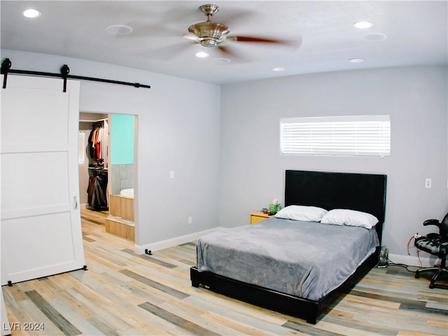 bedroom with baseboards, light wood finished floors, recessed lighting, a walk in closet, and a barn door