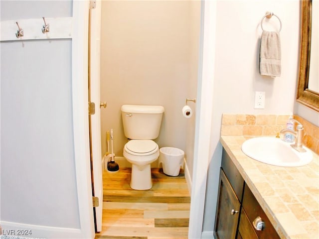 bathroom featuring baseboards, toilet, wood finished floors, and vanity