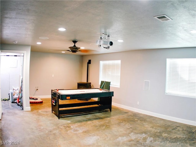 playroom with visible vents, baseboards, concrete flooring, and a wood stove