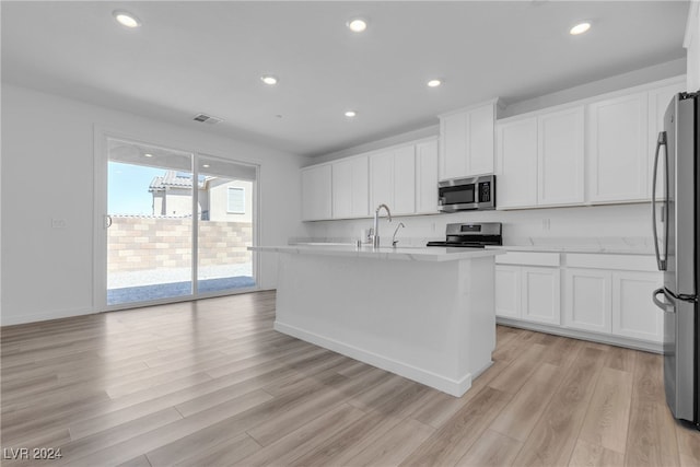 kitchen with an island with sink, stainless steel appliances, light hardwood / wood-style floors, and white cabinetry